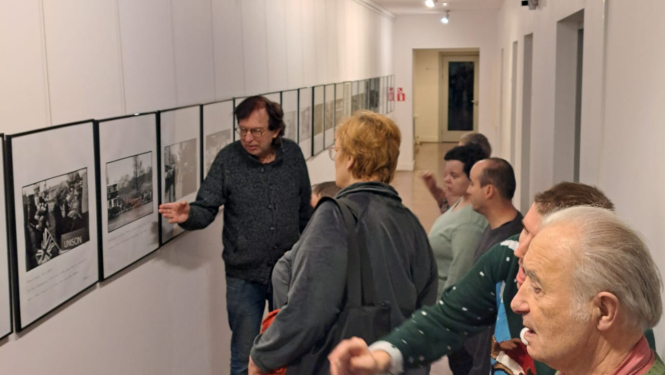 Ļaudis aplūko foto un gleznu izstādi